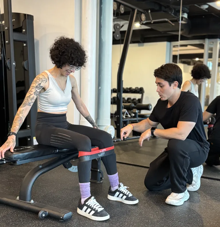 Guilherme kneeling beside a client to guide a banded hip exercise