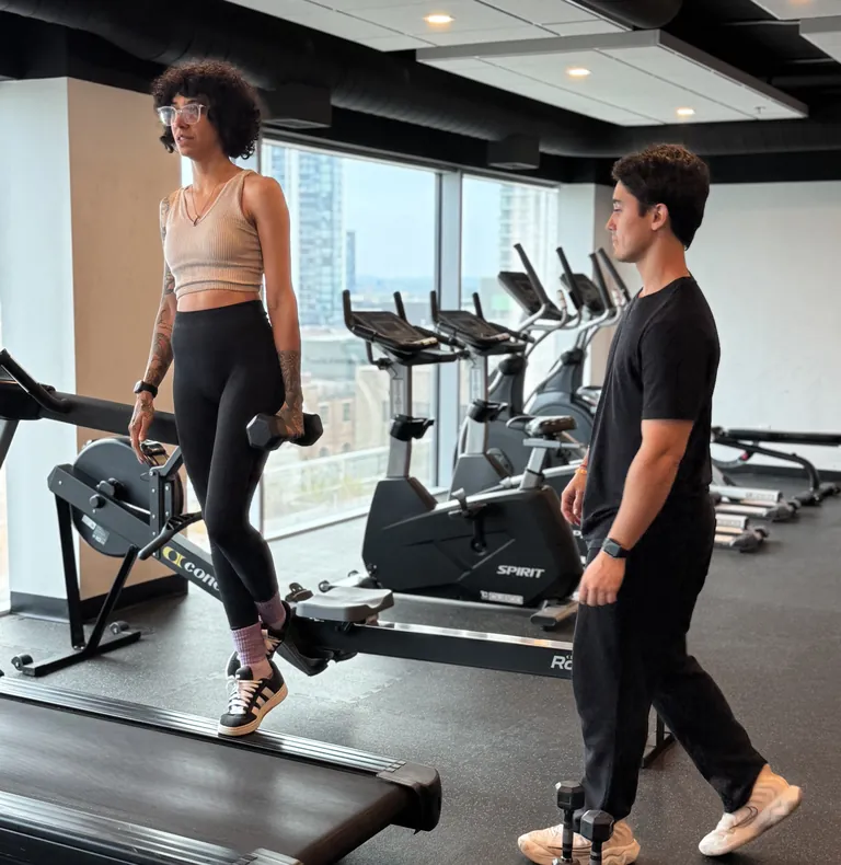 Client walking with dumbbells while Guilherme watches her form